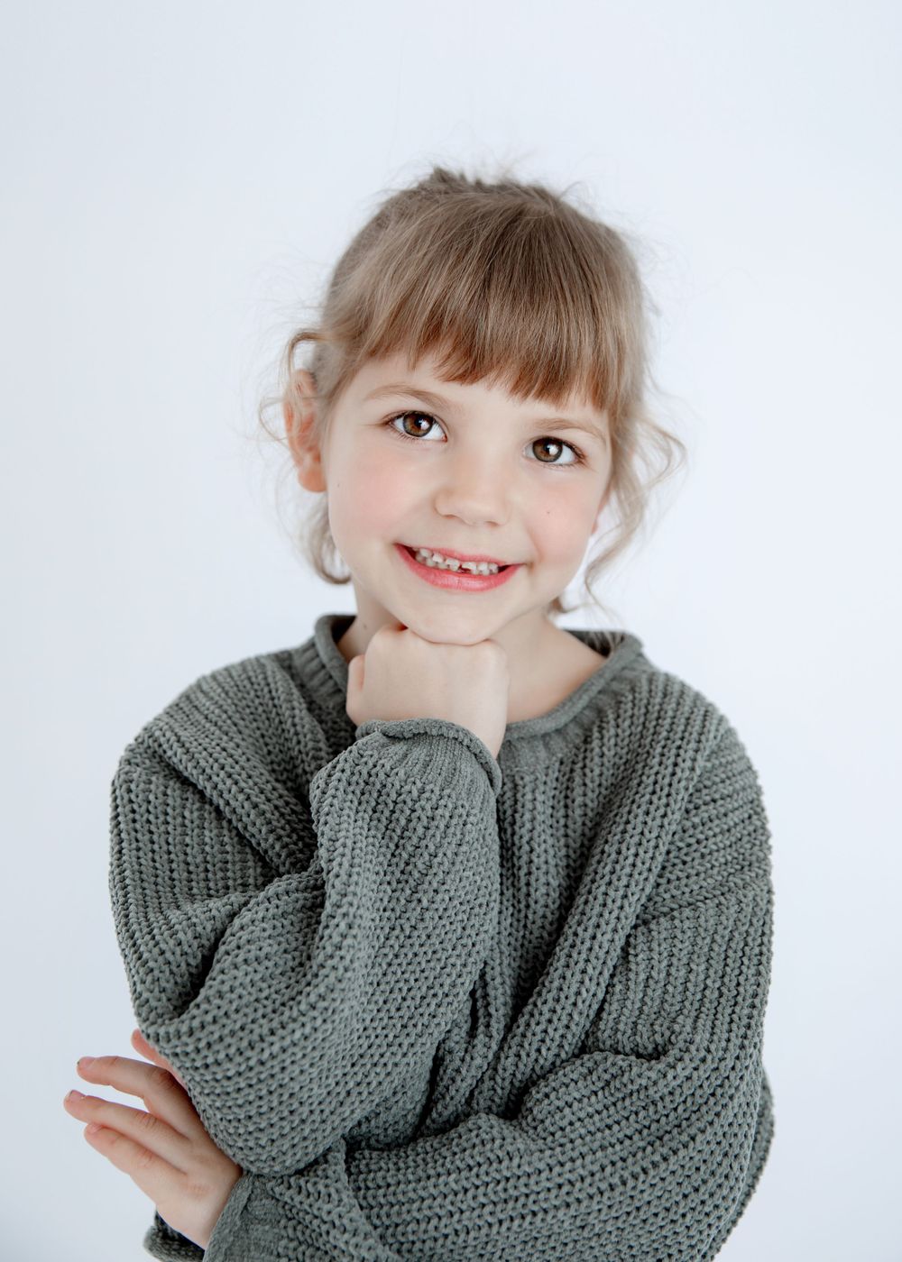 Close-up studio portrait of child wearing gray knit sweater with hand under chin.