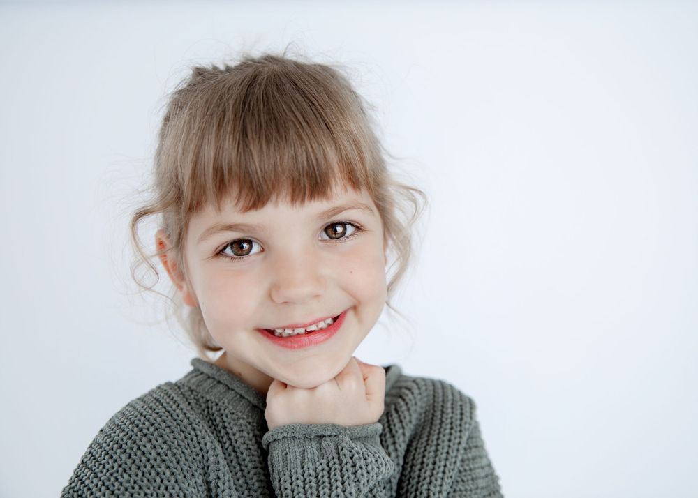 Portrait of child in gray knit sweater with cheerful expression against white background.
