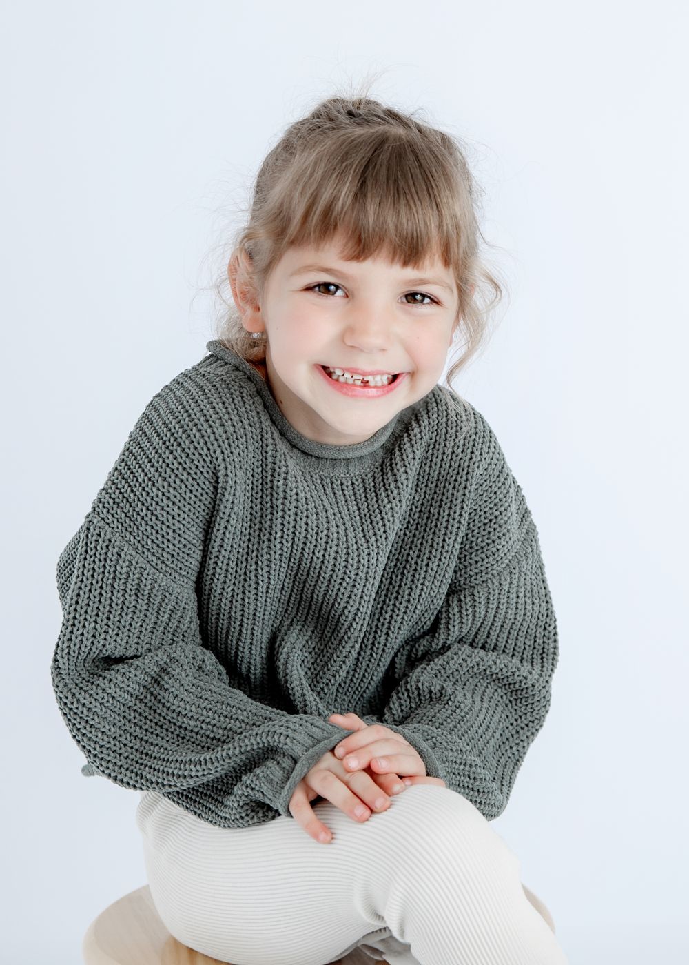 Warm portrait in chunky gray sweater against simple white studio backdrop.