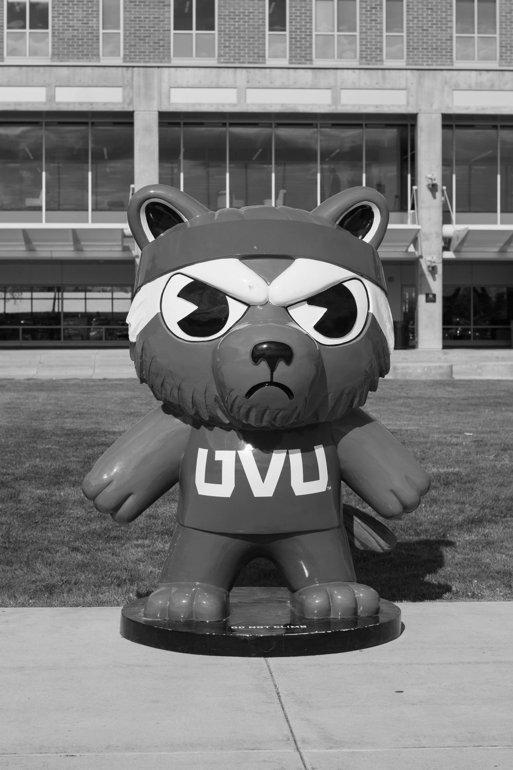 A large black inflatable mascot character wearing a UVU shirt stands outside a brick building in black and white.