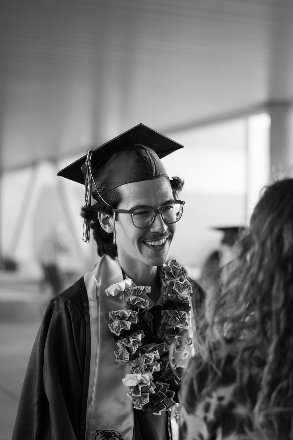 A joyful graduate wearing a black cap and gown with a floral lei at commencement.