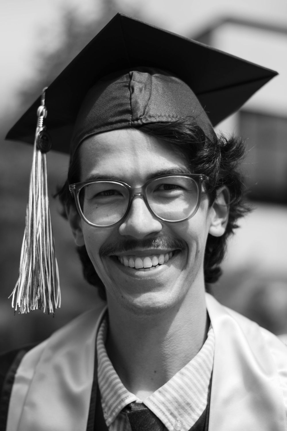 Graduate in cap and gown with glasses smiles in black and white portrait.