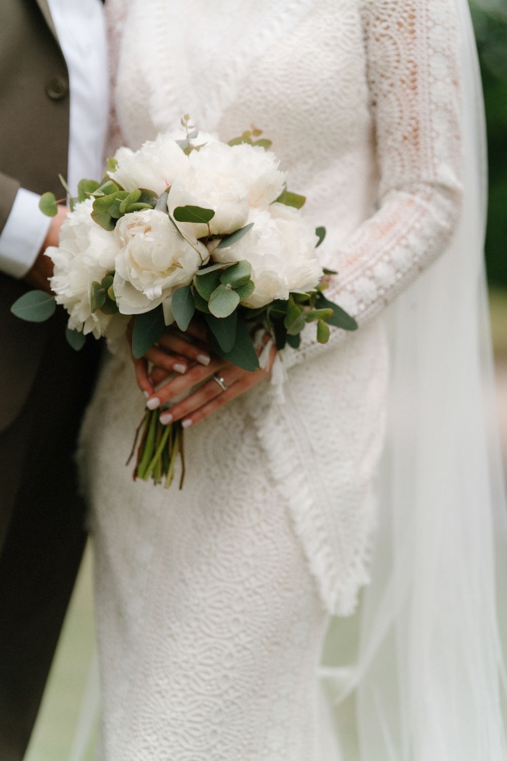 Close-up of white lace wedding dress with delicate floral bouquet.
