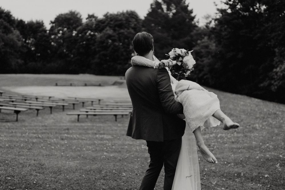 A couple in wedding attire dances together in a grassy field with picnic tables in the background.