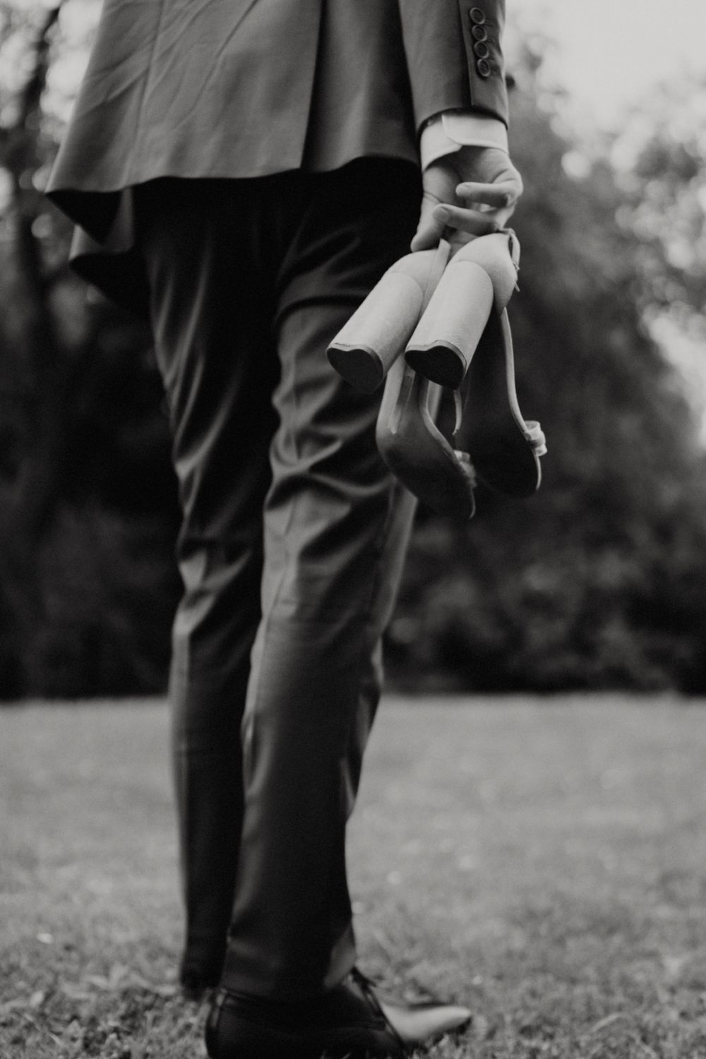 Detail shot of formal black dress shoes and pants on grass during an outdoor event.