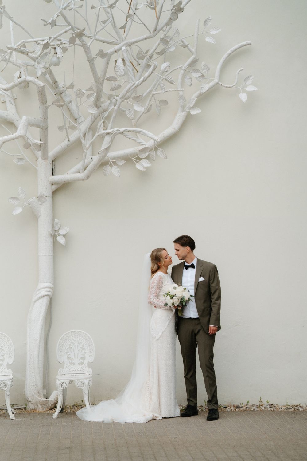 Artistic wedding portrait against a white wall with decorative white tree branches.