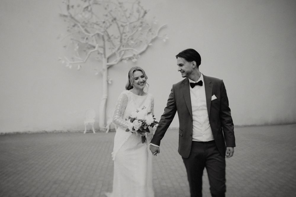 Black and white wedding portrait featuring decorative white tree installation against stark wall.