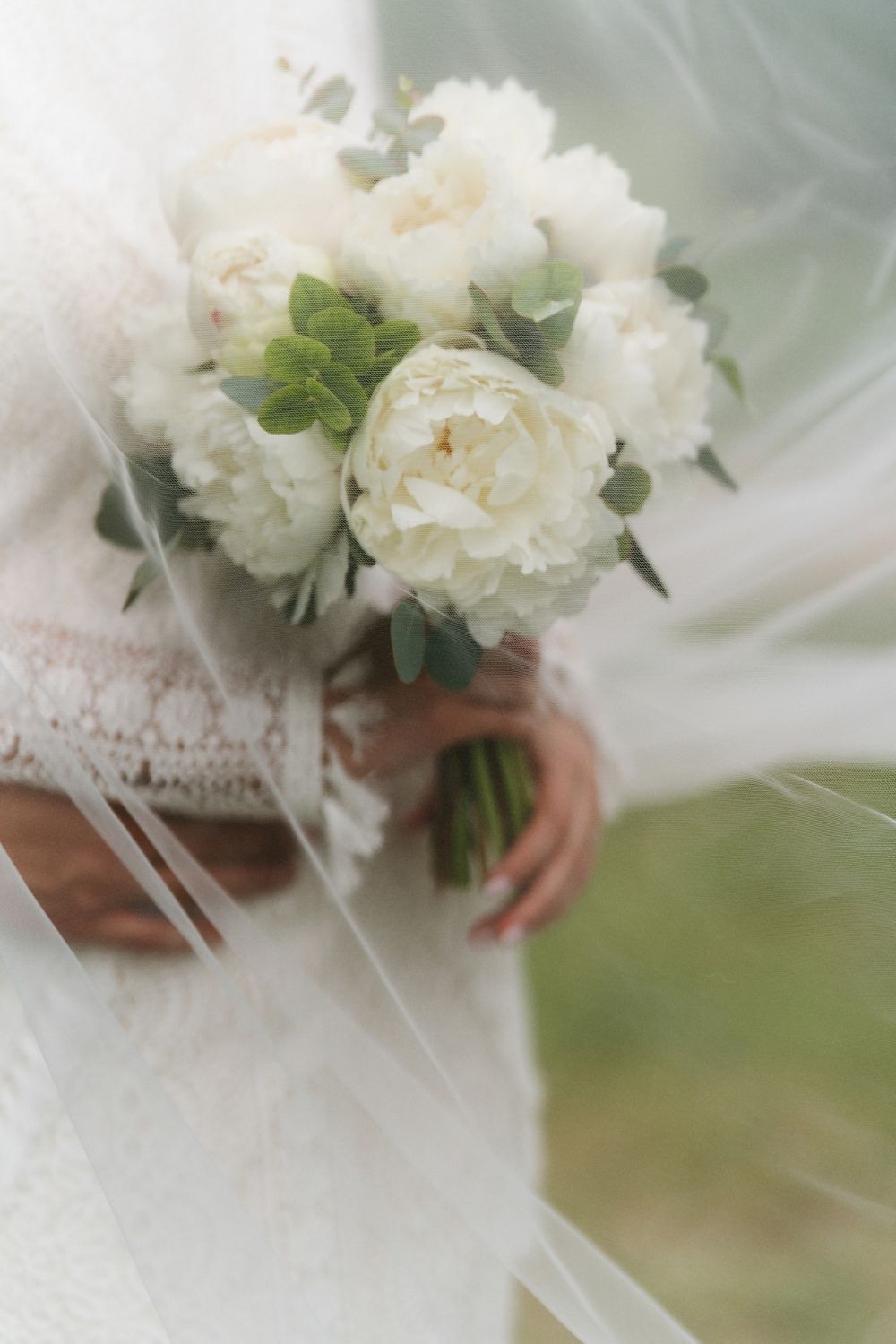 Delicate white floral bouquet wrapped in lace and held by hands against a soft blurred background.