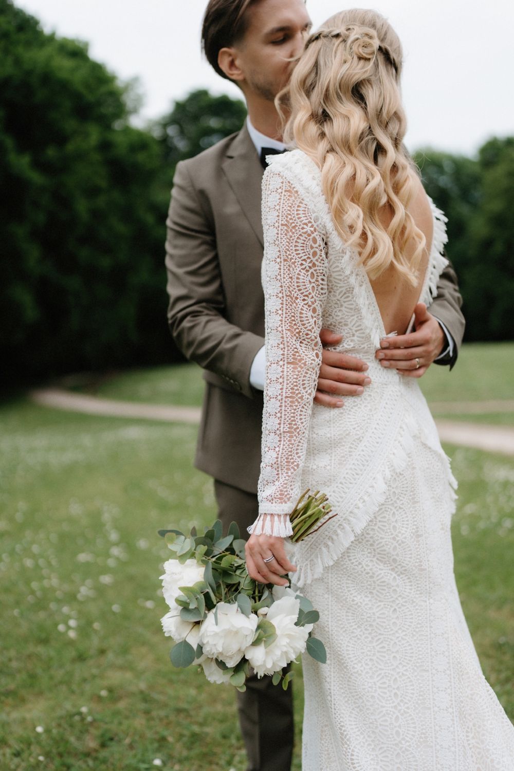 Elegant long-sleeved lace wedding dress with white bouquet photographed outdoors.