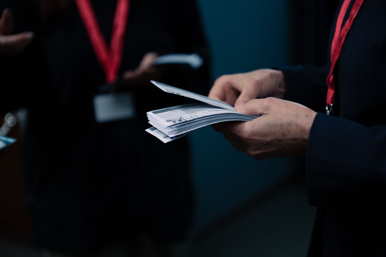 Close-up of hands holding papers in dimly lit conference setting.