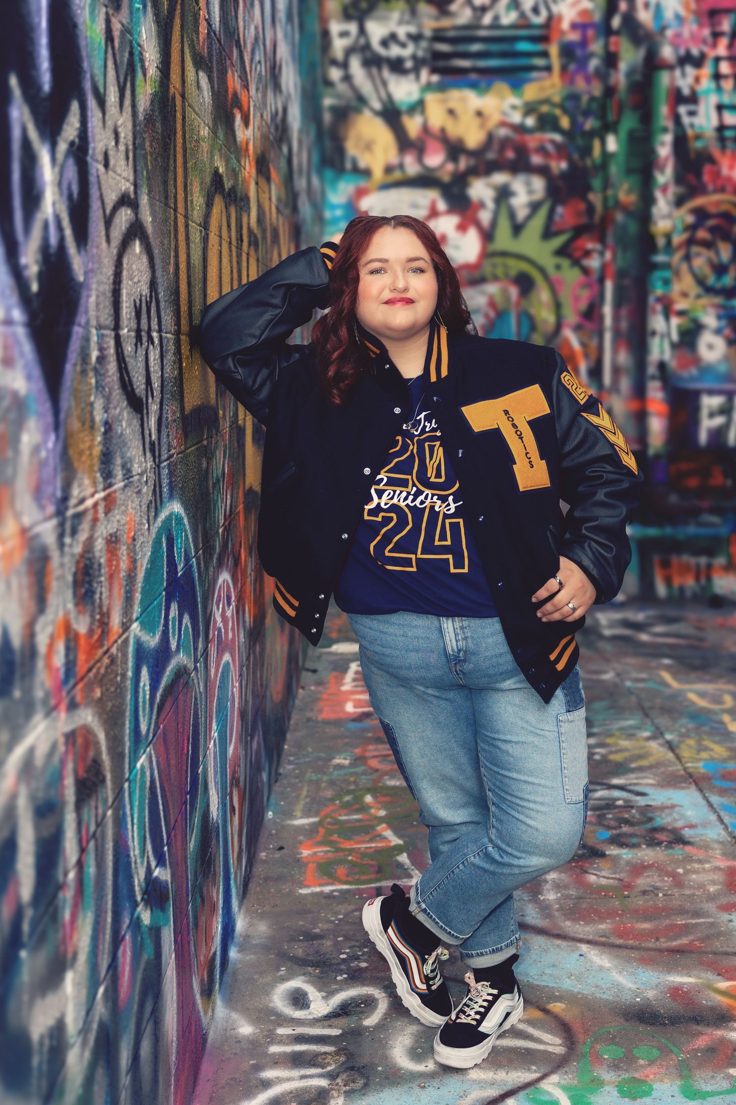 Urban portrait against colorful graffiti walls wearing varsity jacket and jeans.