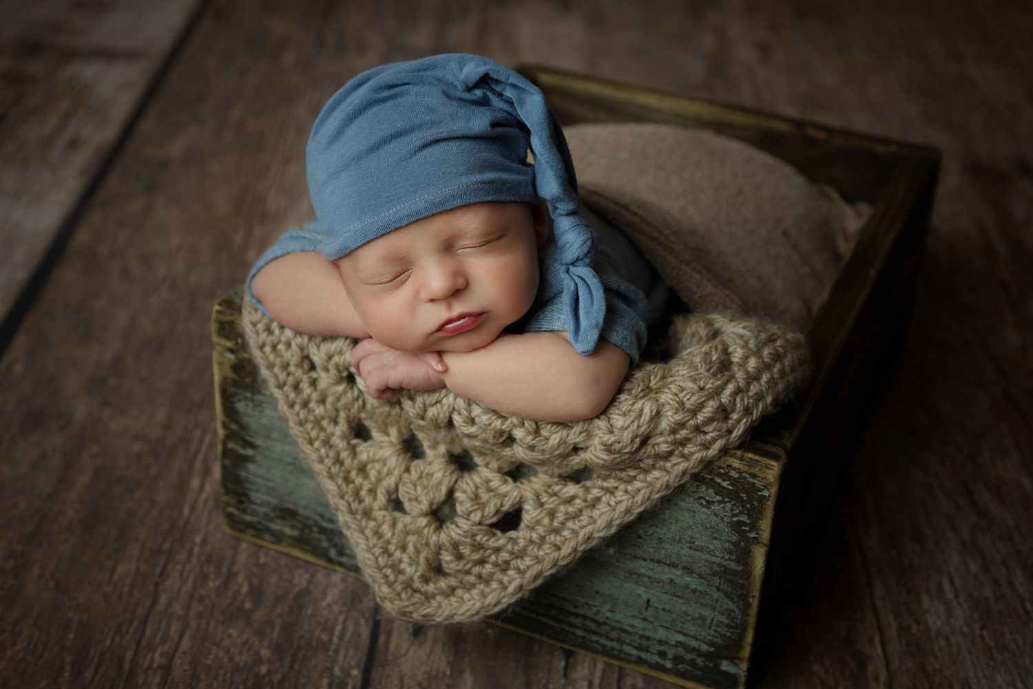 A peaceful newborn boy peacefully sleeping in a rustic wooden crate, surrounded by soft blankets.