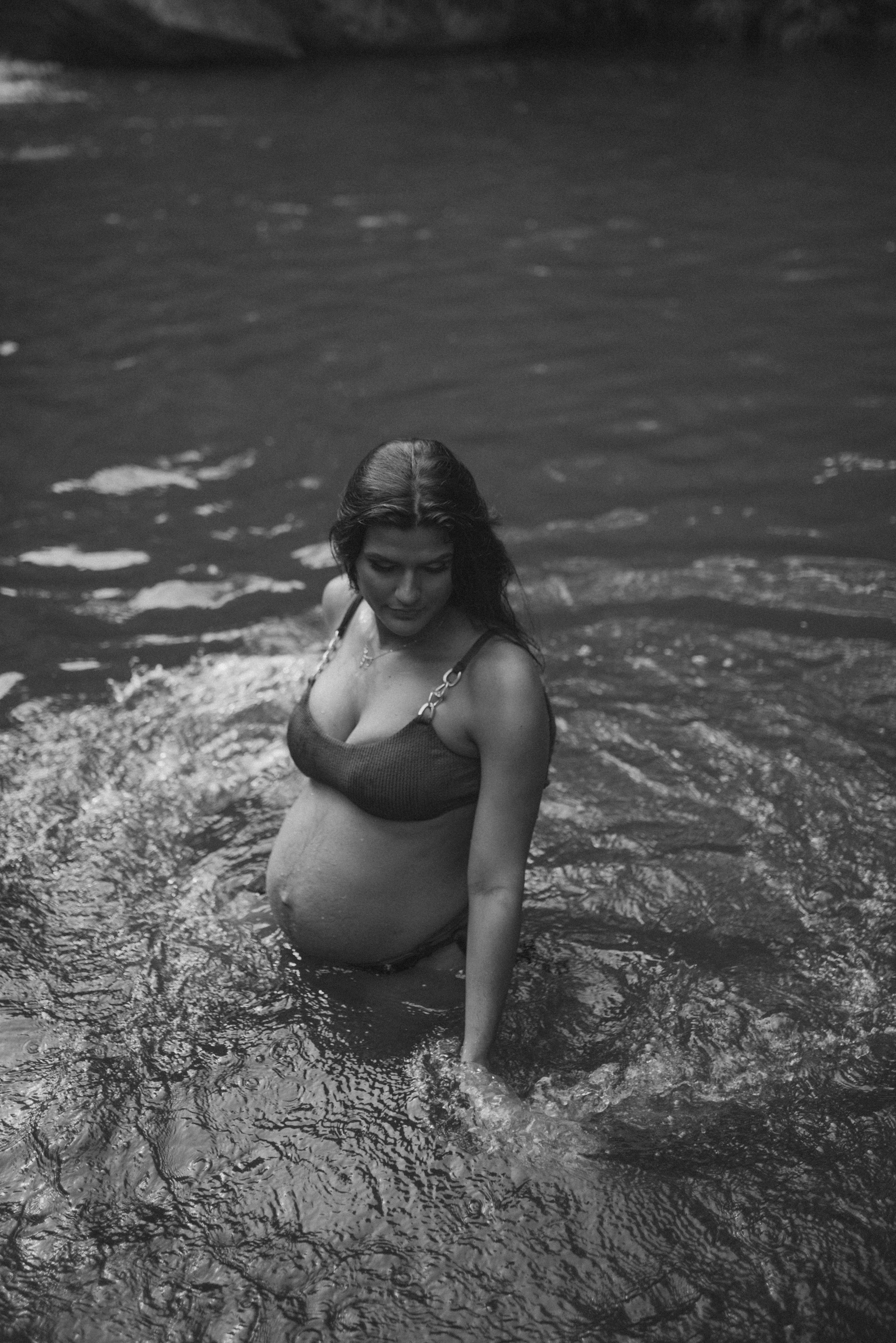 Black and white photo of an expecting mother enjoying time in the water wearing a bikini.
