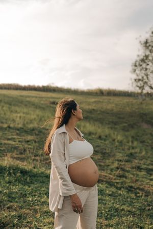 Pregnant person in white outfit standing in grassy field during golden hour.