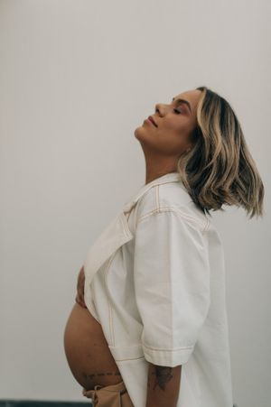 Side profile of pregnant woman in white denim jacket against neutral background.