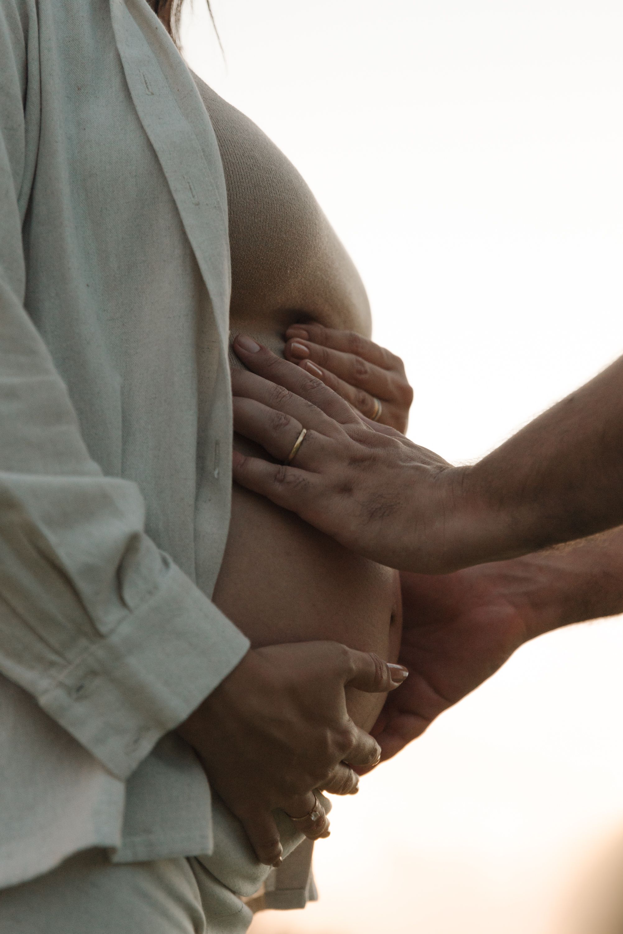 Close-up of hands tenderly cradling a pregnant belly in soft lighting.