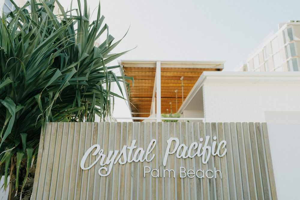 Crystal Pacific Palm Beach signage on wooden wall with tropical plants.
