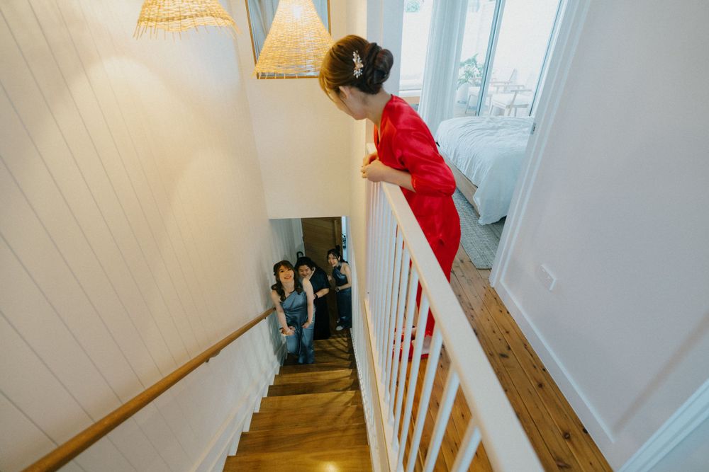 A child in red peeks down a wooden staircase with white railings.