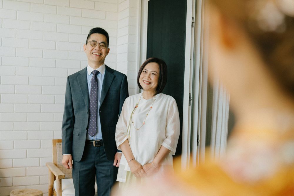 A couple stands together near a white brick wall in formal attire at a special event.