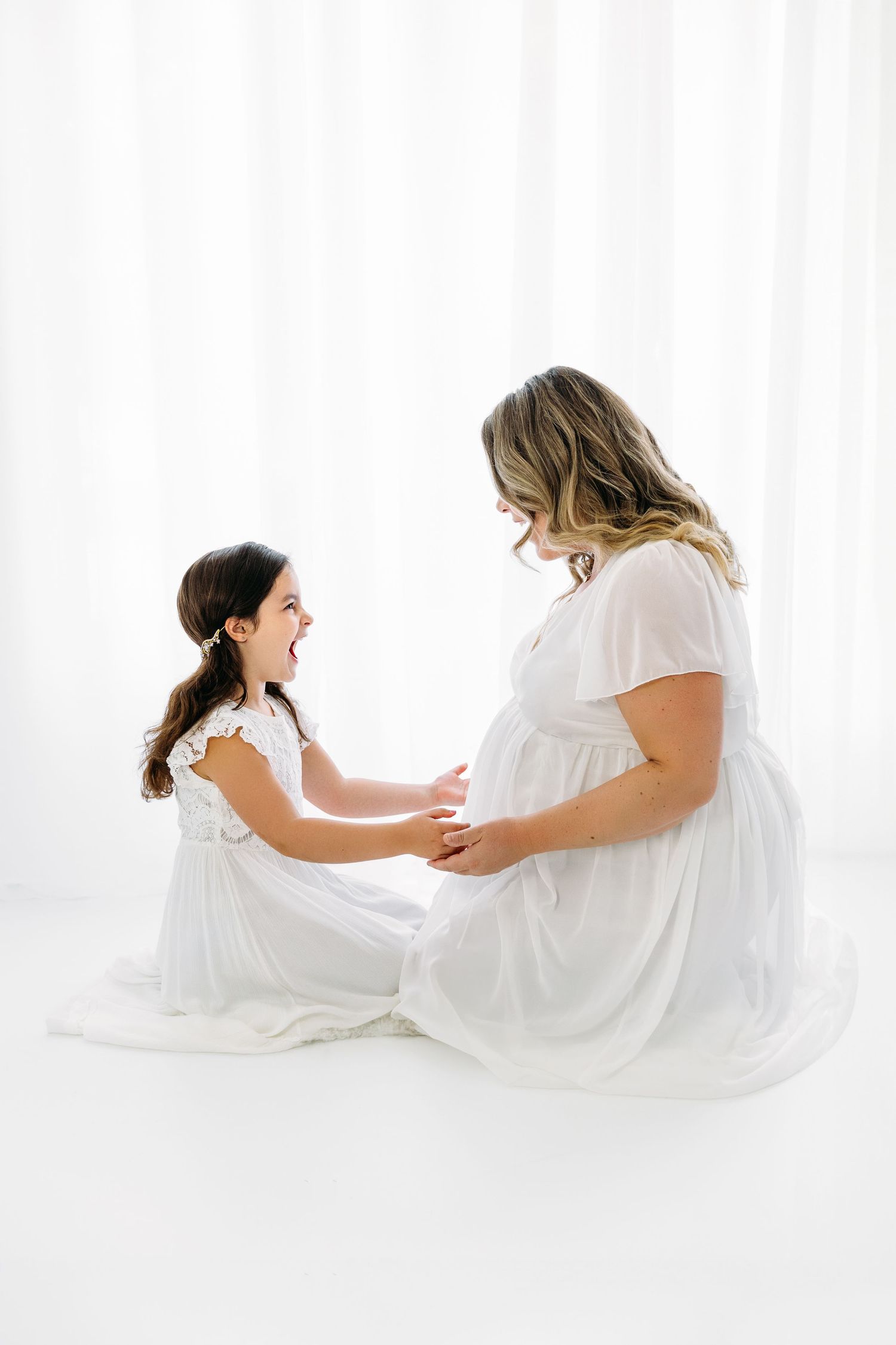 Mom and 6 year old daughter kneeling together, excited about Mom's pregnancy