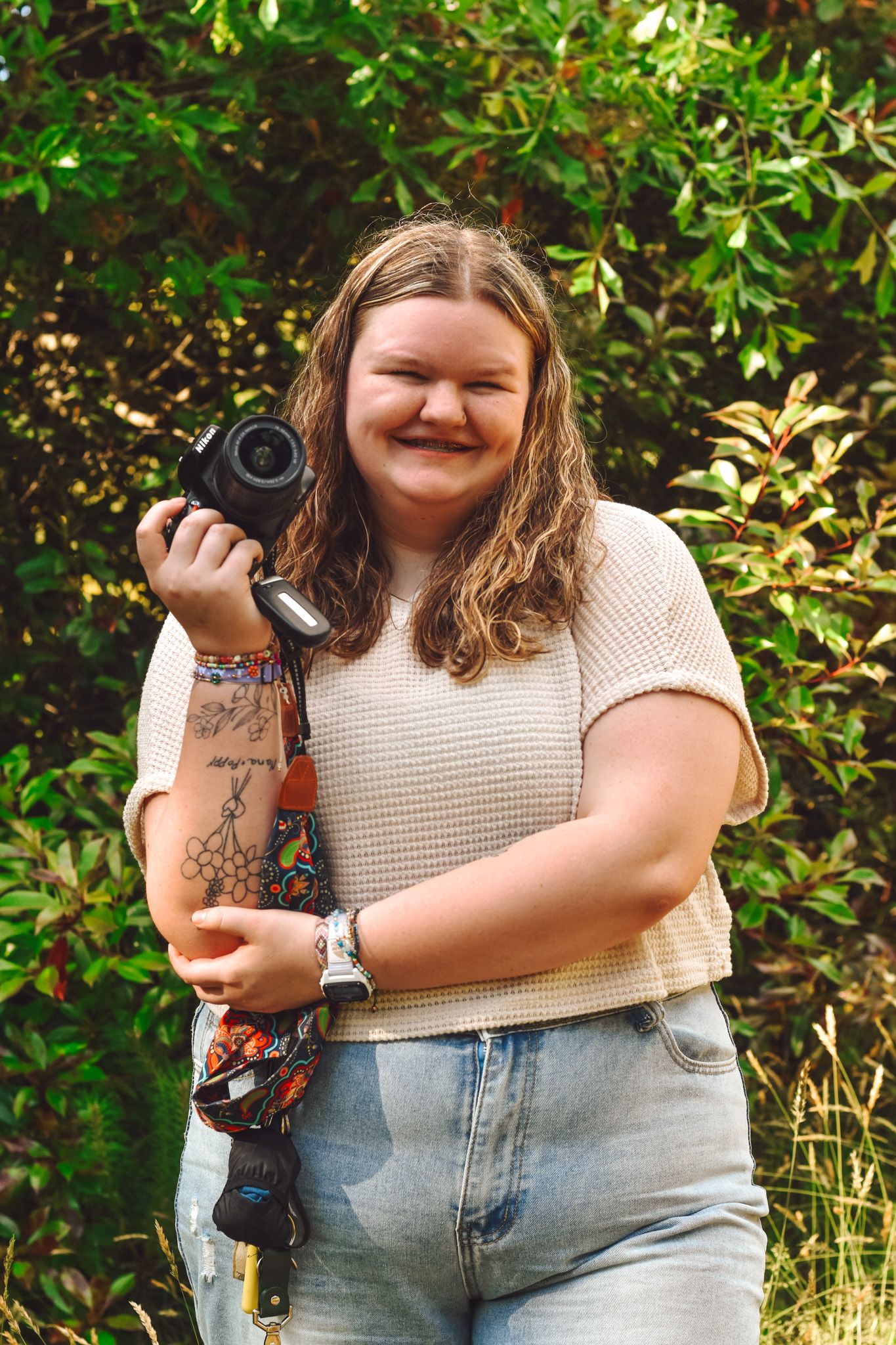 Person holding professional camera outdoors with leafy green background.