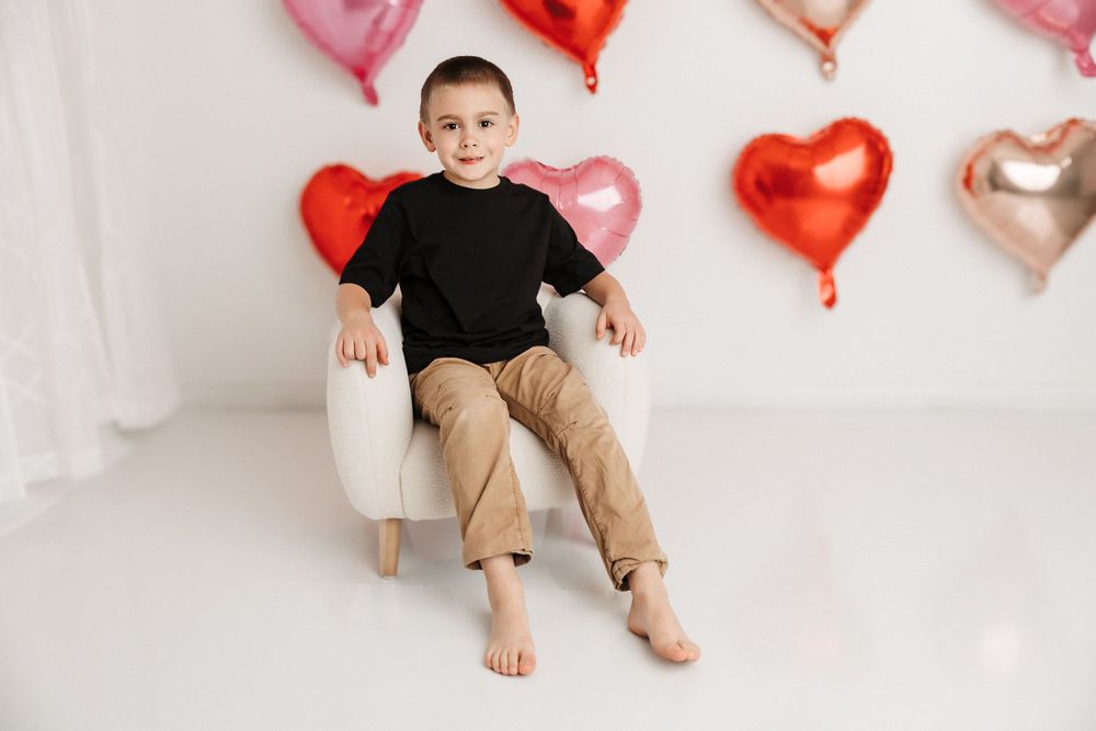Valentine's Day mini session boy sitting on white chair with pink and red heart balloons- Kayla Decker Photography LLC