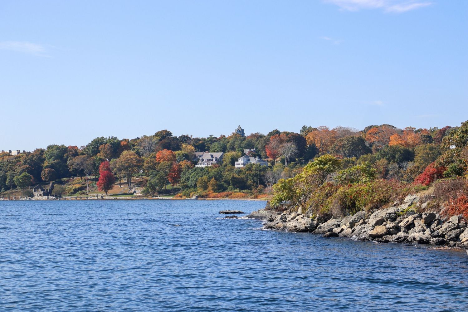 Autumn colors along rocky coastline with waterfront homes visible on hillside.