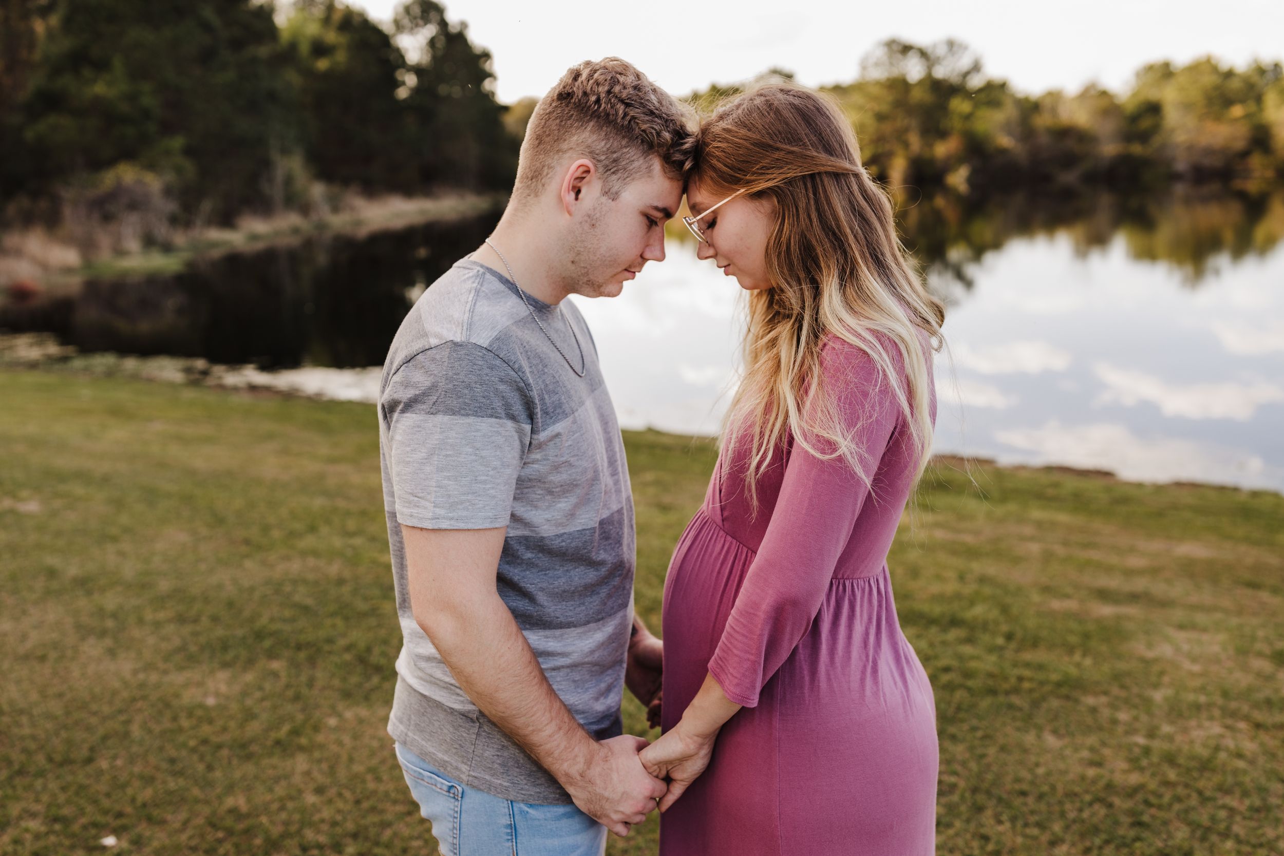 A tender moment between a couple outdoors with a lake in the background.