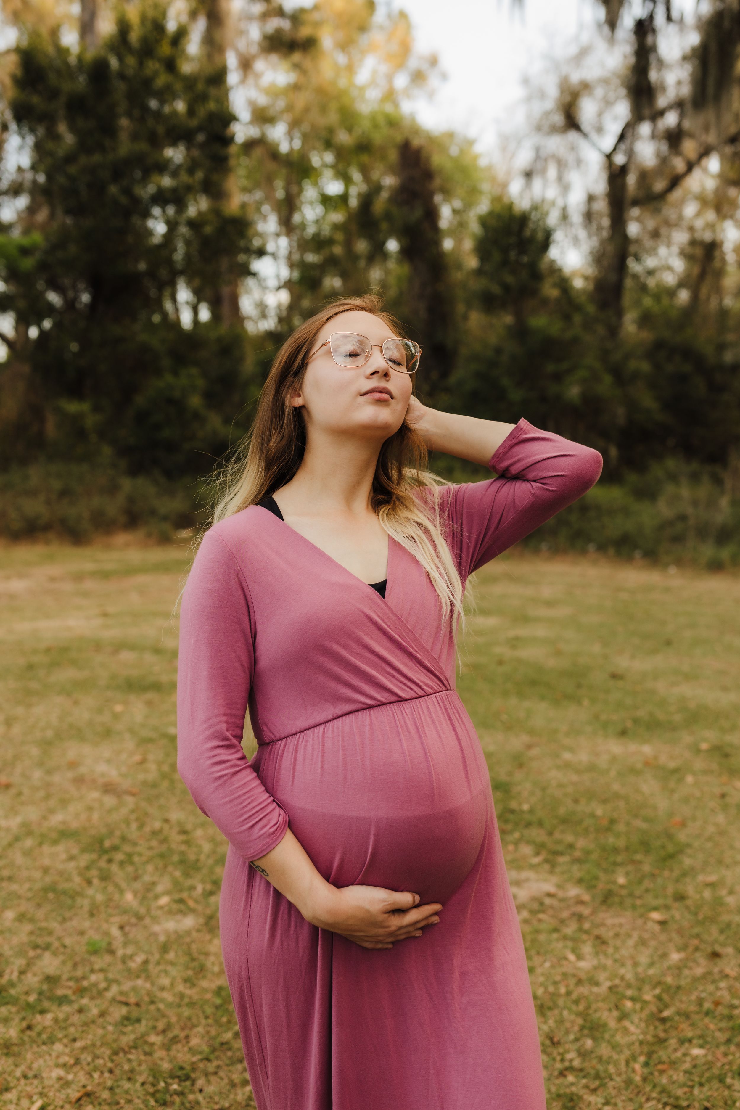 A serene maternity portrait of a woman in pink dress enjoying a peaceful moment outdoors.