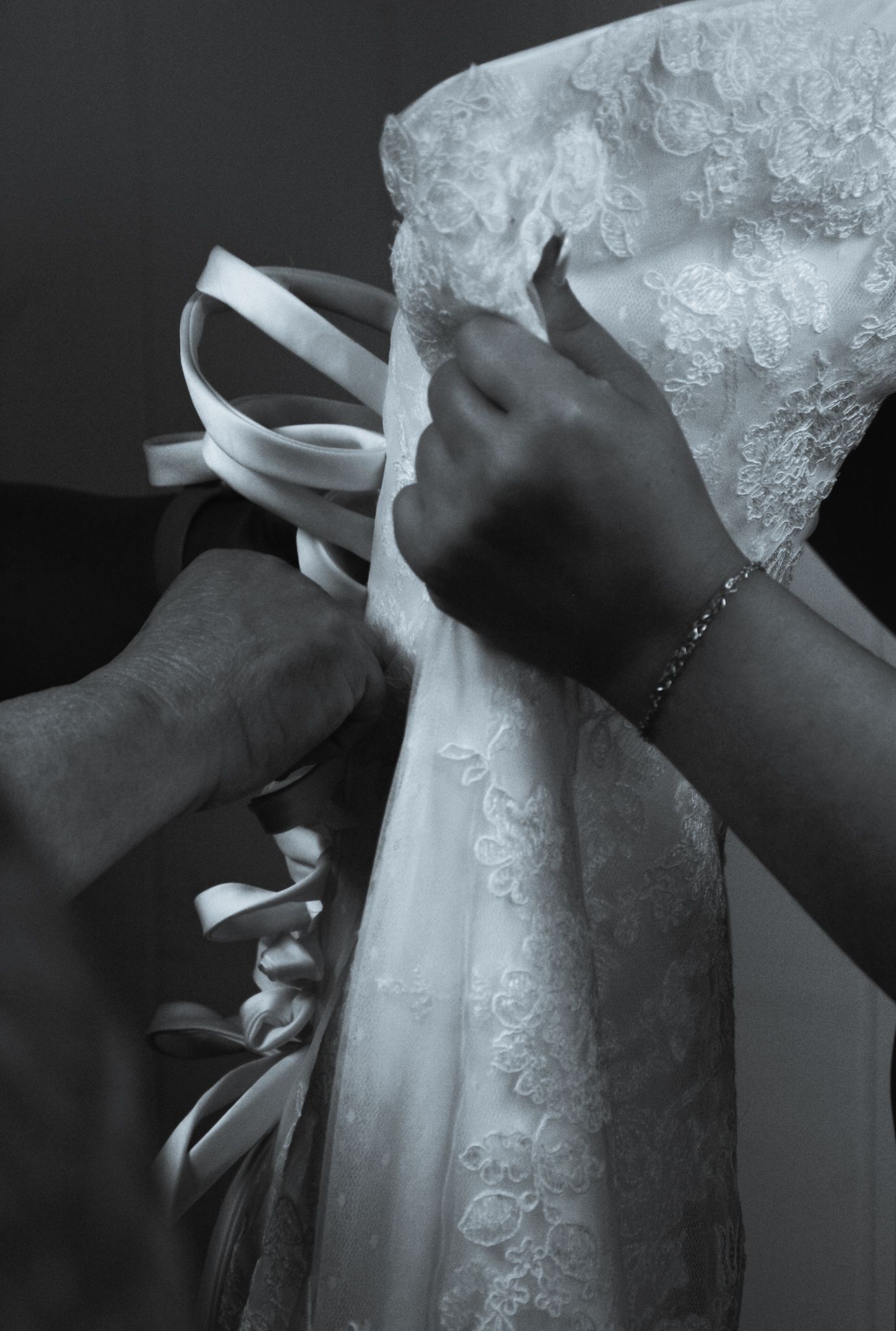 Hands adjusting a white lace wedding dress in black and white photography.