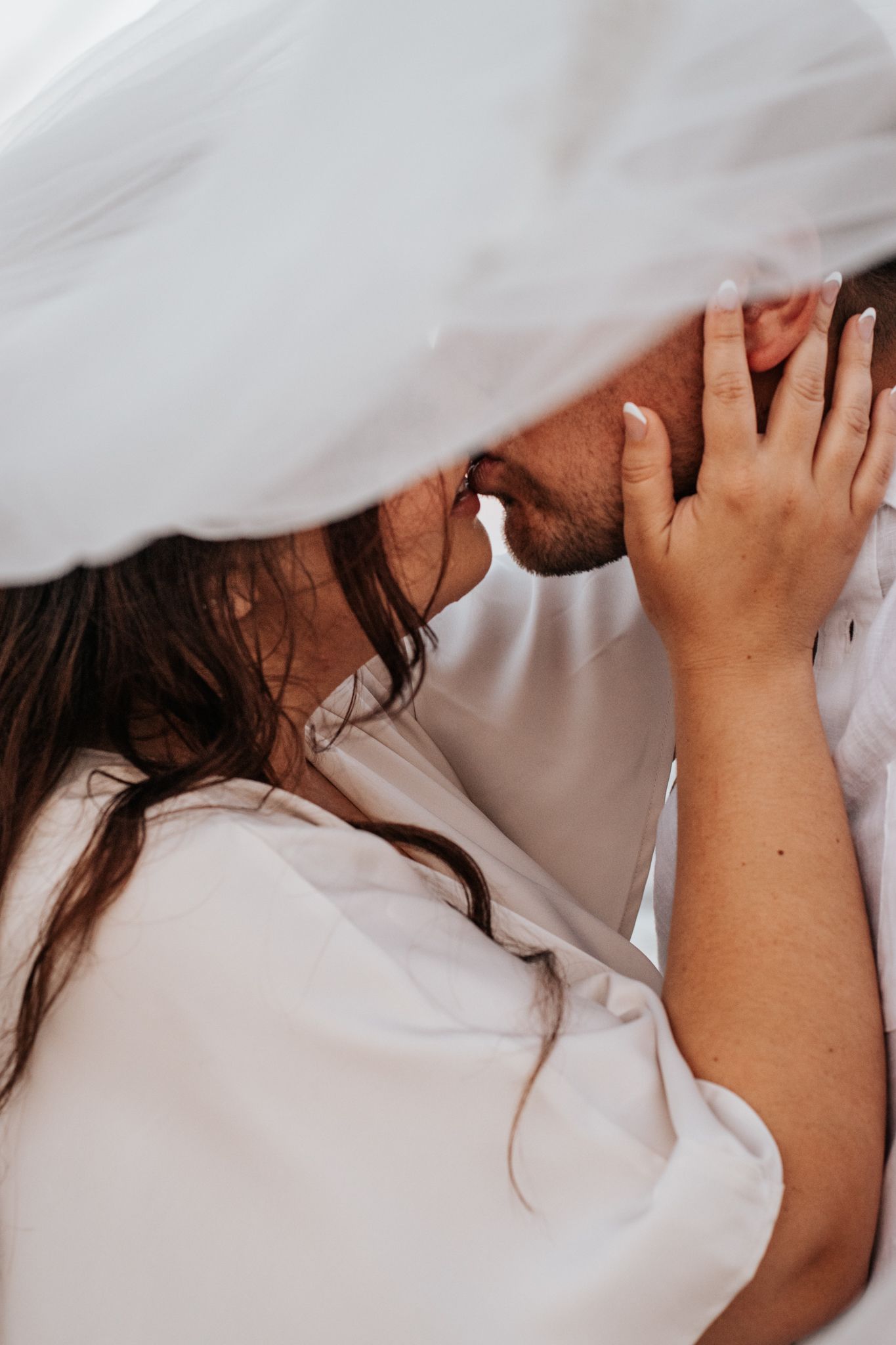 Romantic couple sharing tender moment under flowing white fabric.