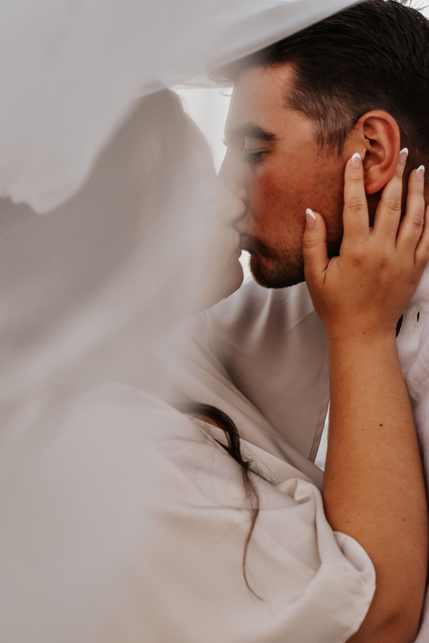 Intimate portrait under white fabric with hands touching face.
