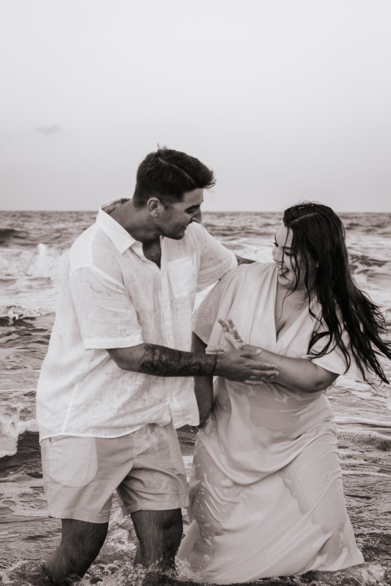 Playful couple in white clothing dancing in the ocean waves.
