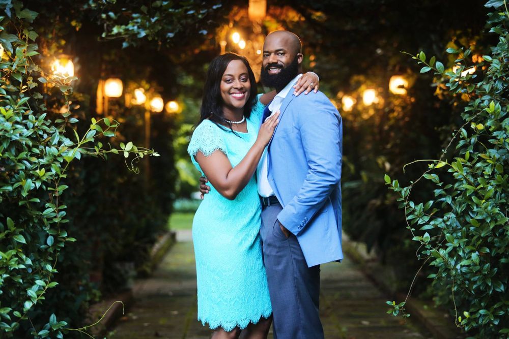 A couple poses in a garden pathway lit by glowing lanterns at dusk.