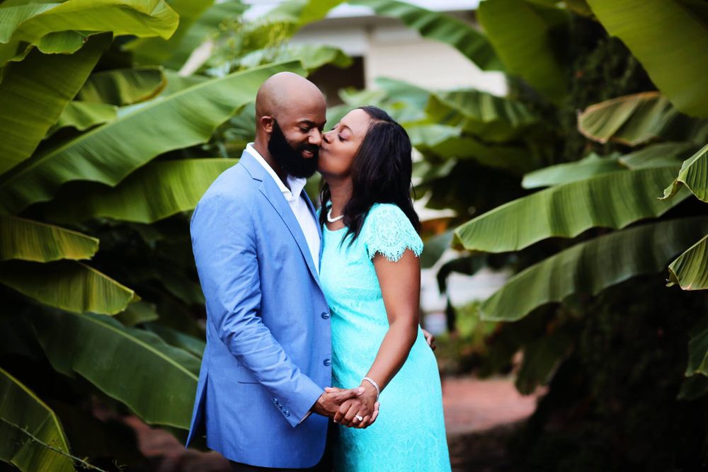 A couple embraces among tropical plants wearing blue formal attire.