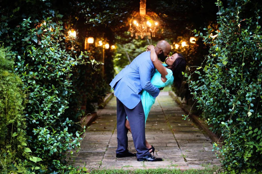 A romantic couple embraces on a garden path illuminated by glowing lanterns at dusk.