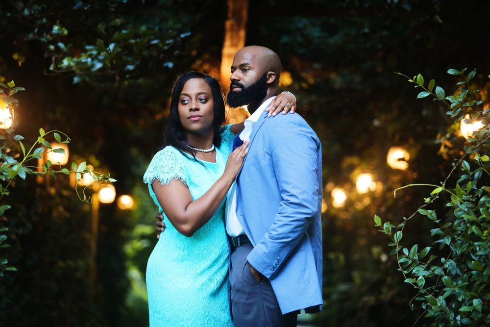 A couple in blue and turquoise formal wear poses in an evening garden with twinkling lights.
