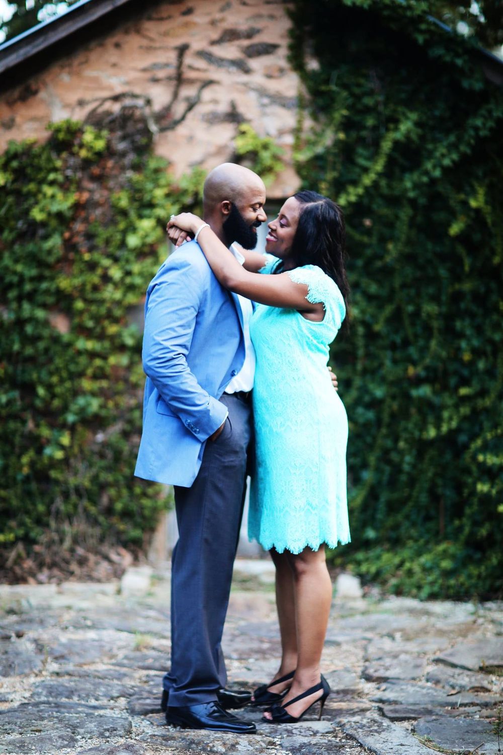 A couple shares an intimate moment on a stone pathway with ivy-covered walls.