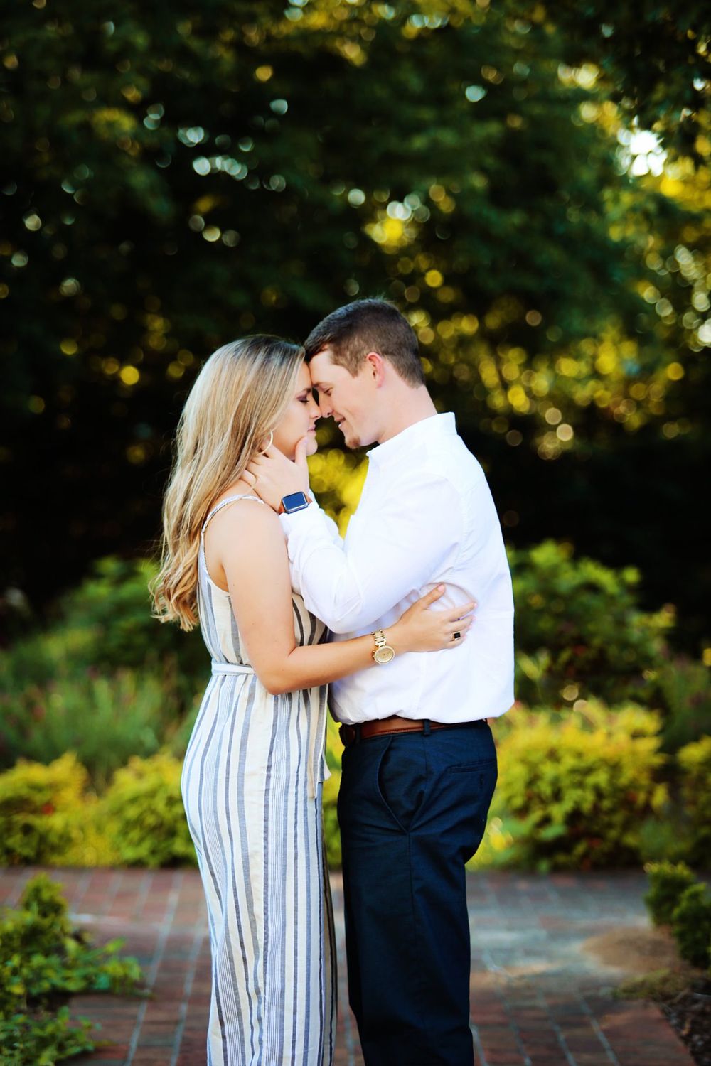 A couple in casual attire shares a tender moment in a sunlit garden setting.