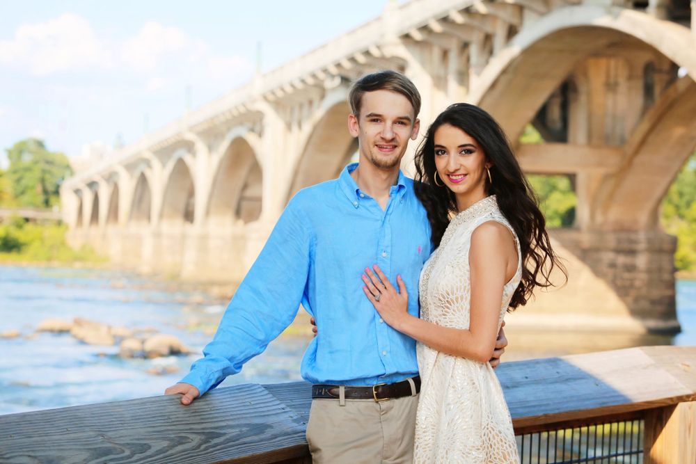 A couple poses together near a historic bridge on a sunny afternoon.
