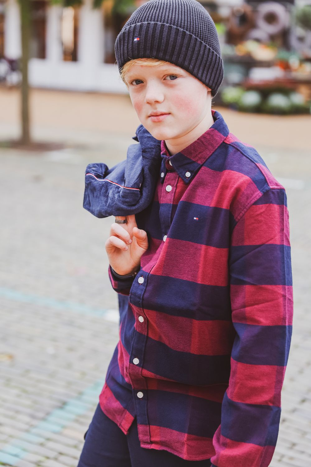 Portrait in red and navy striped shirt and beanie against urban background.