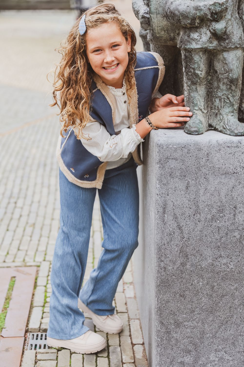 Casual pose leaning against stone statue base wearing denim and white blouse.