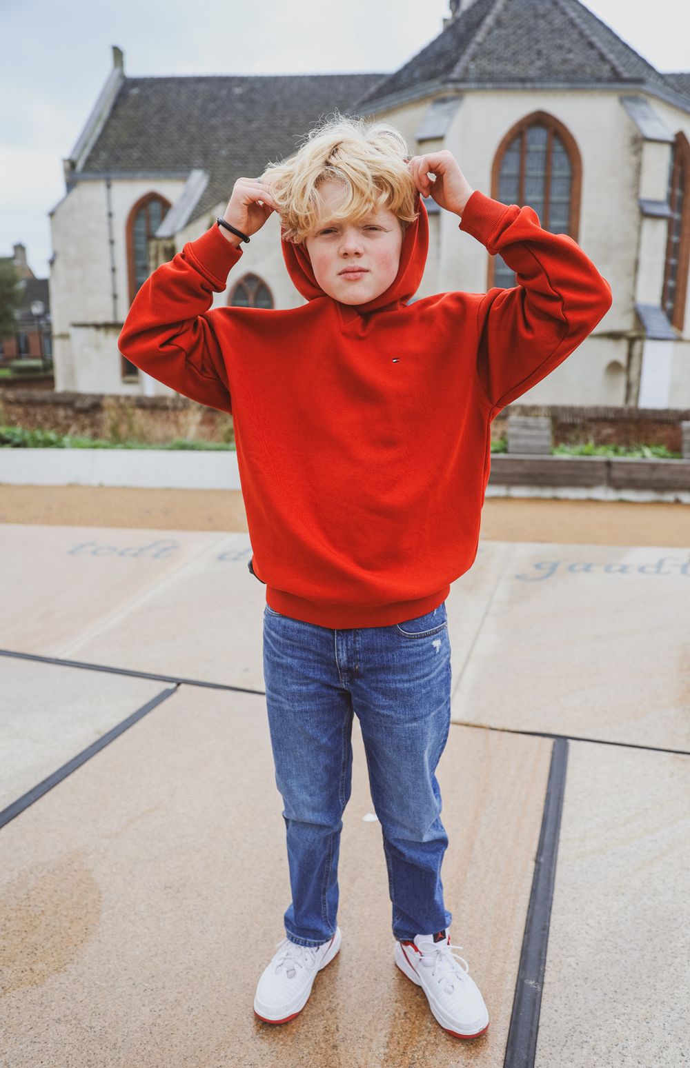 Standing pose in bright red sweater and jeans with church building in background.
