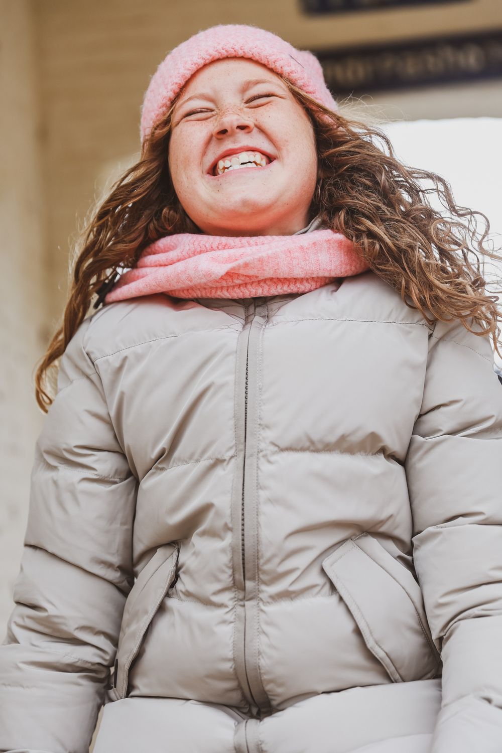 A joyful winter moment captured wearing a pink beanie, scarf and gray puffer jacket.