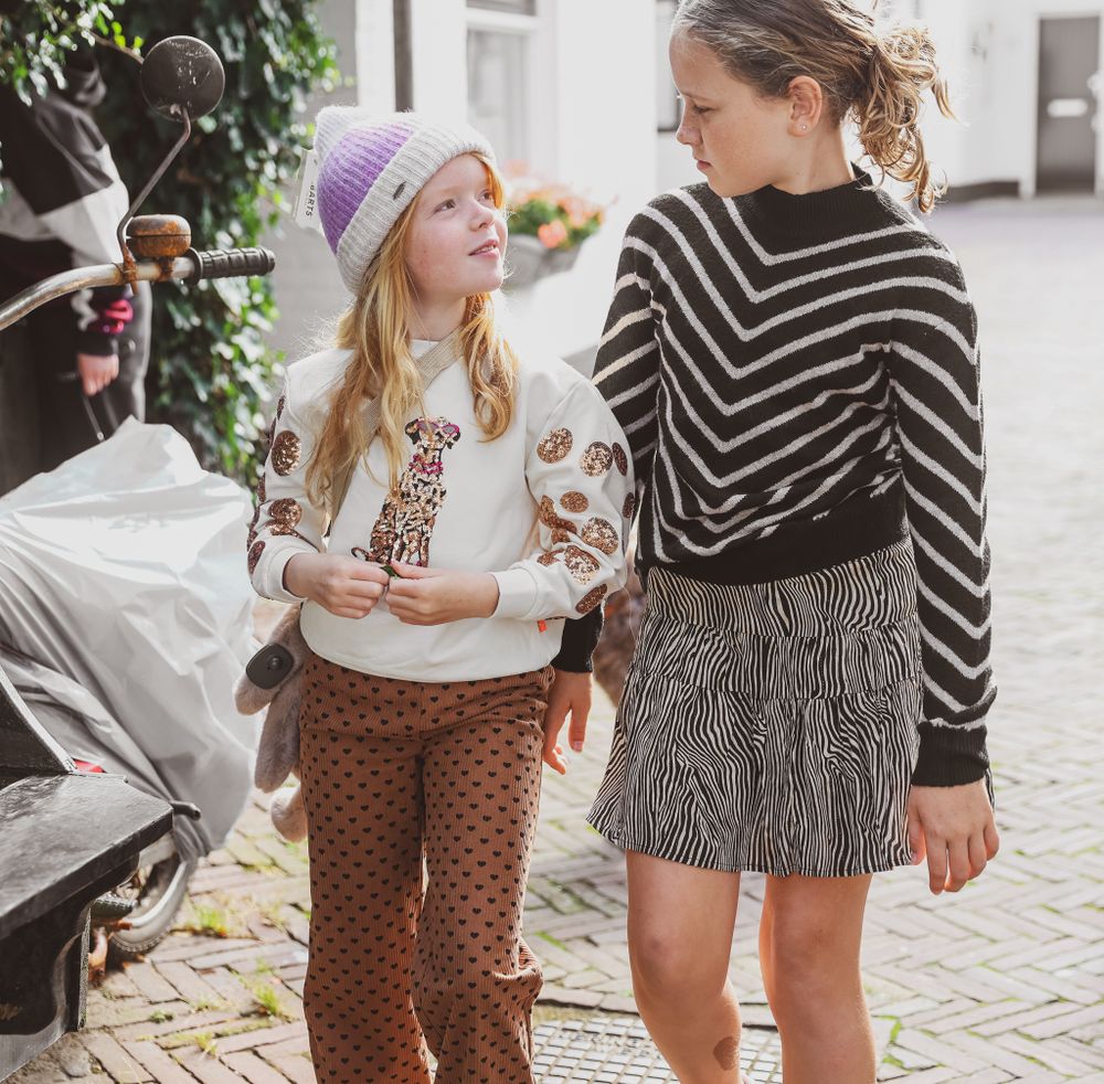 Two friends in stylish winter outfits chatting on a cobblestone street.
