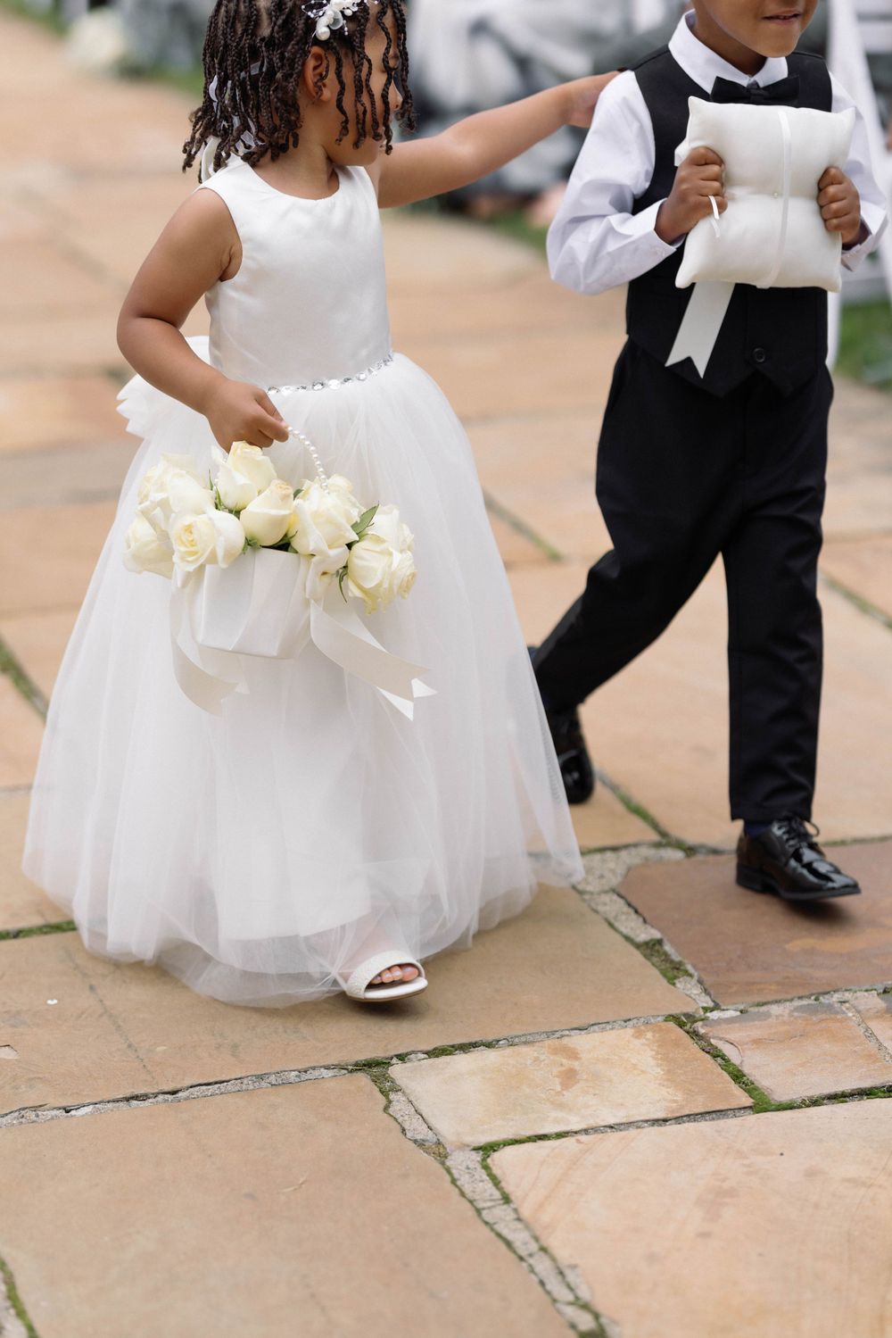 Young flower girl in white dress holds bouquet next to ring bearer in formal attire.