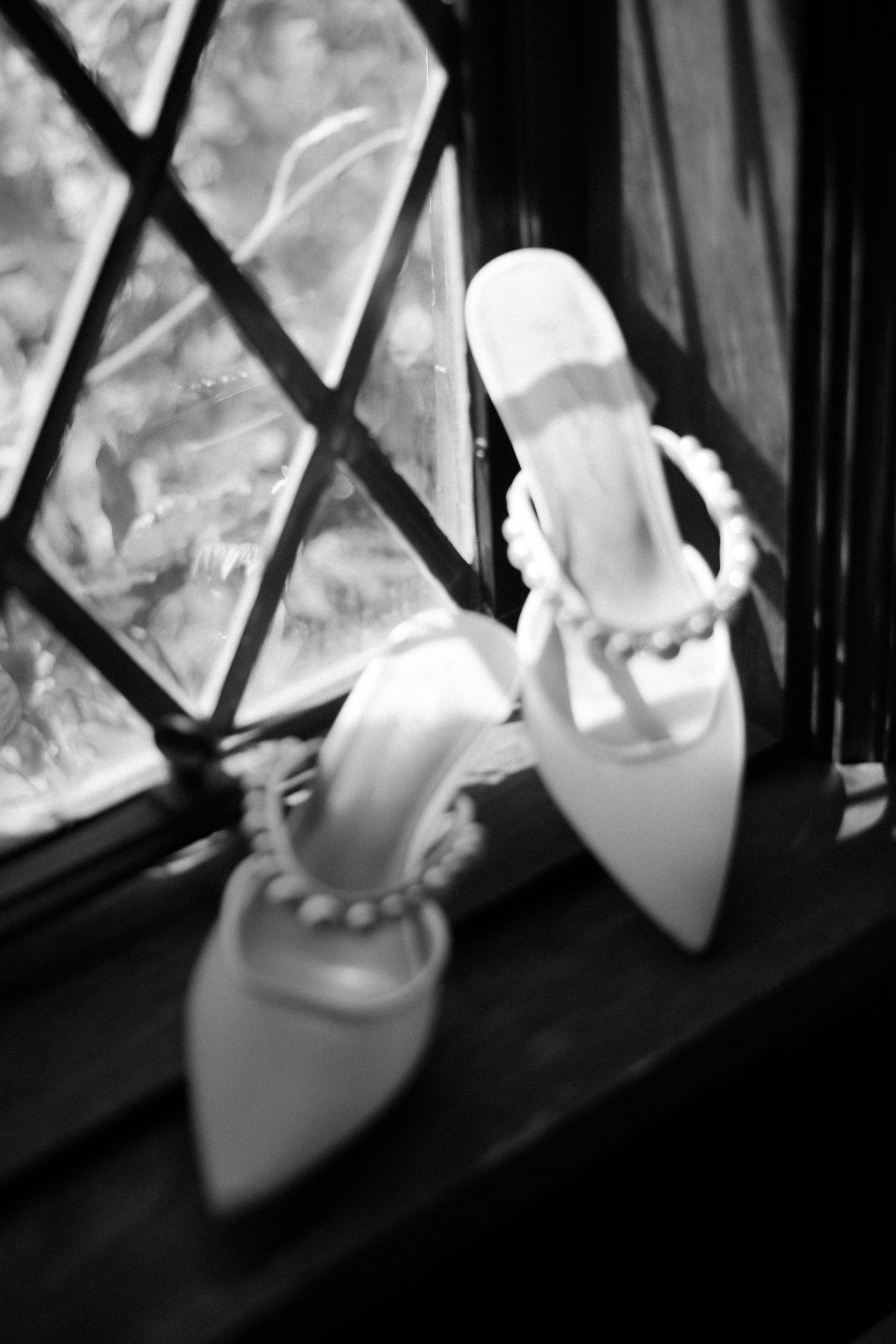 Elegant white bridal shoes with pearl details sitting on a windowsill in soft focus.