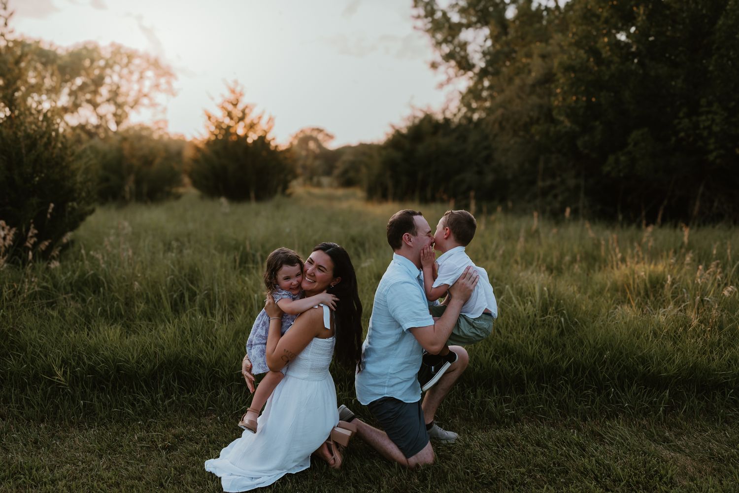 Two couples embrace in a sun-drenched field during golden hour. Colorado Springs Photographer.