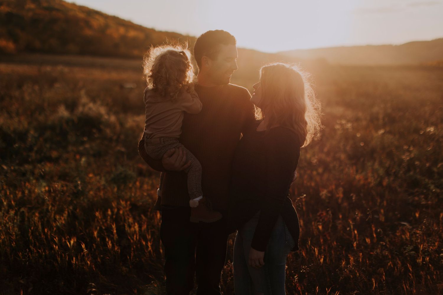 Silhouettes of a family embrace during golden hour in a meadow.