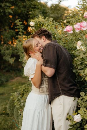A couple shares a tender embrace beside blooming pink roses in a romantic garden at sunset.